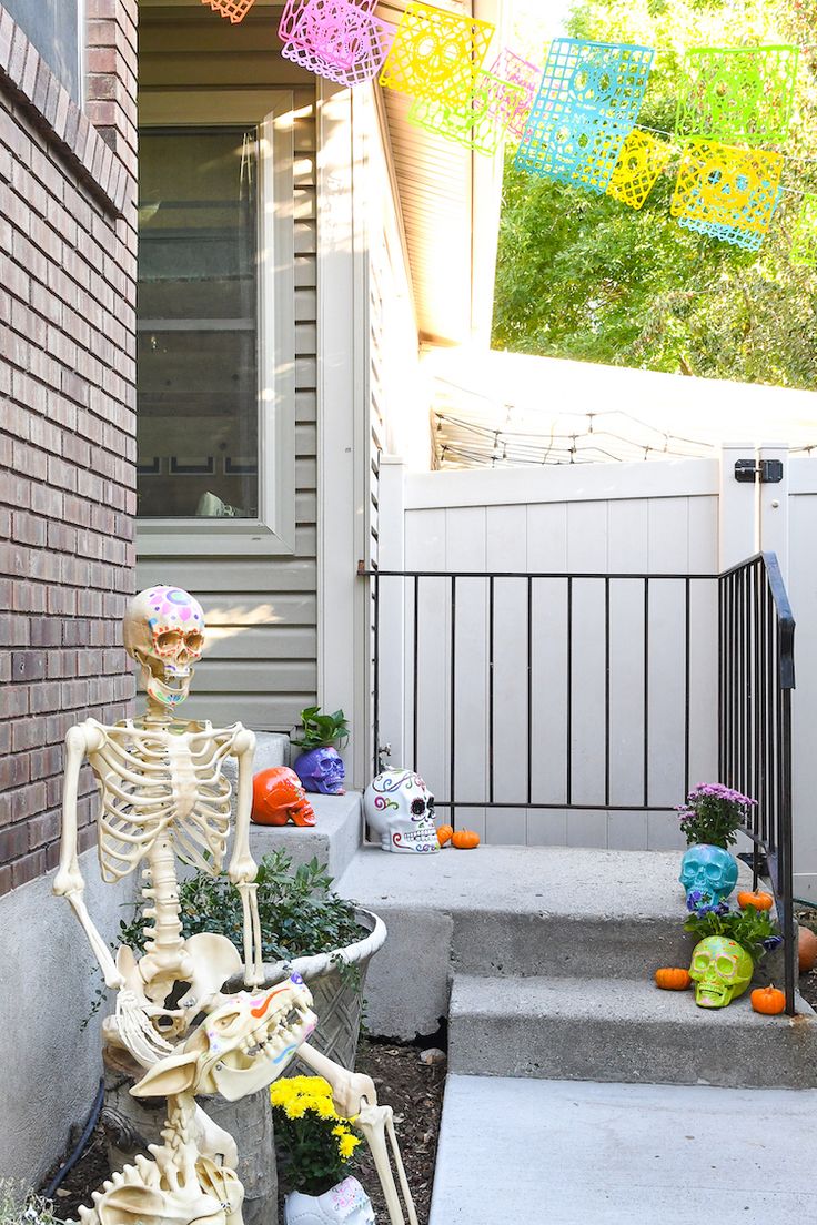 a skeleton statue sitting on top of a planter in front of a house with halloween decorations around it