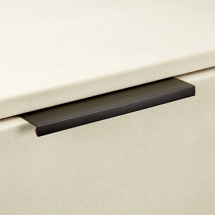 a close up of a drawer handle on a white leather cabinet with black trimming