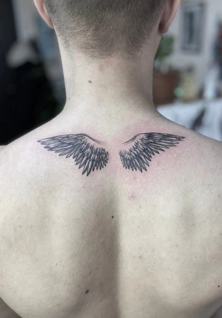 the back of a man's neck with an angel wing tattoo on his chest