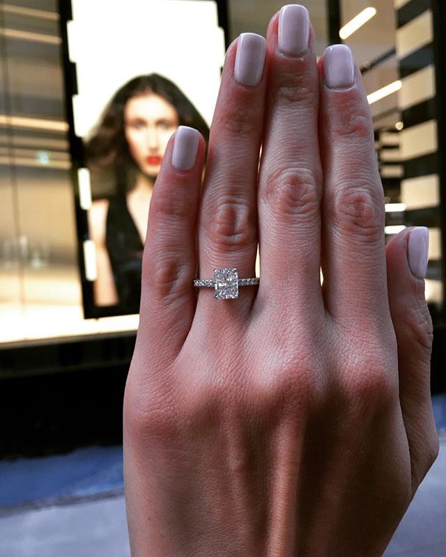 a woman's hand with a diamond ring on her left hand and a television in the background