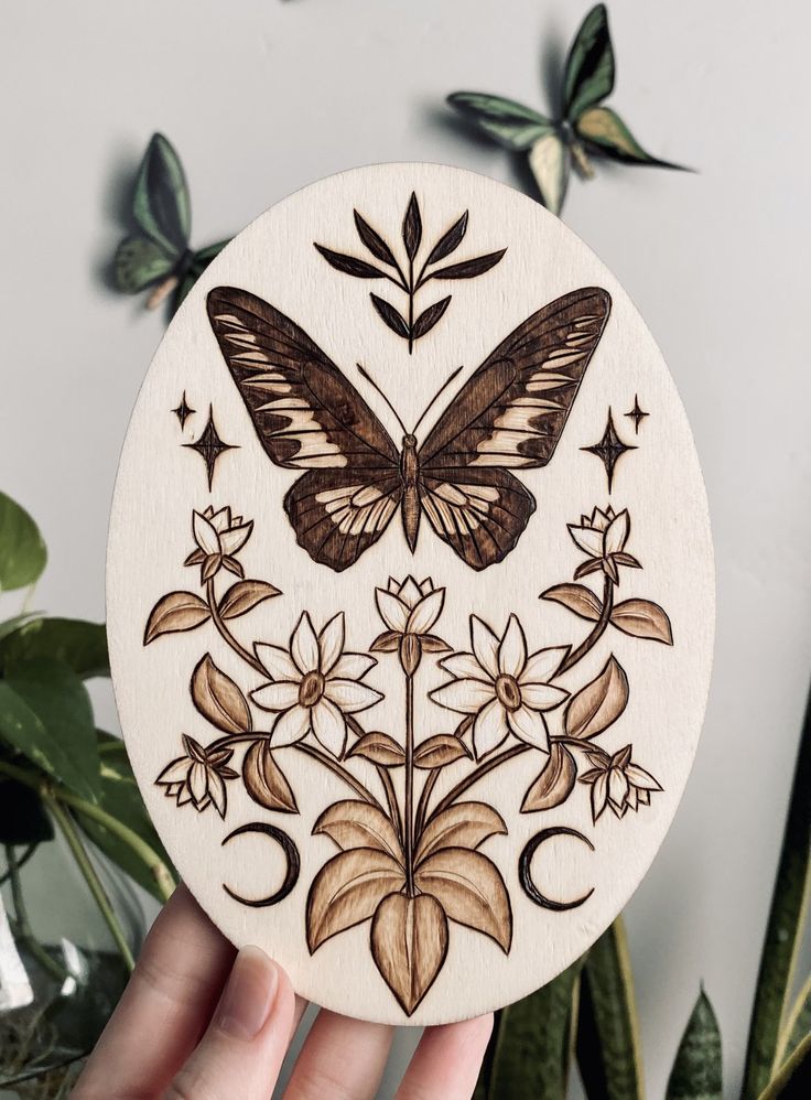 a hand holding up a wooden plaque with a butterfly and flowers painted on the front