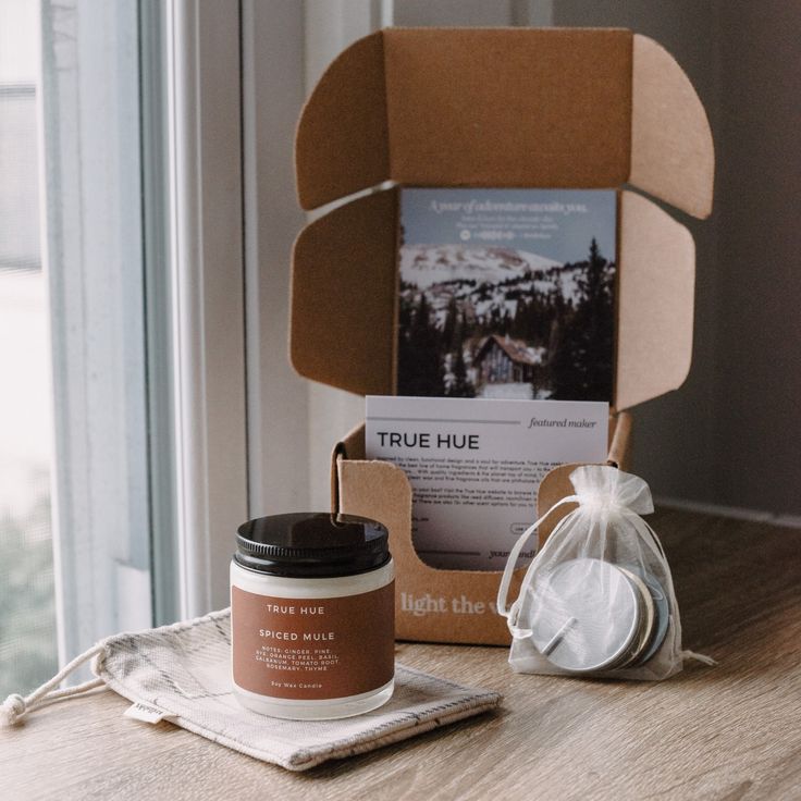 an open box with a candle and some other items sitting on a table near a window