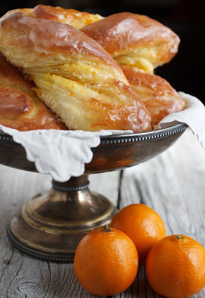 some oranges are sitting on a table next to pastries in a silver bowl