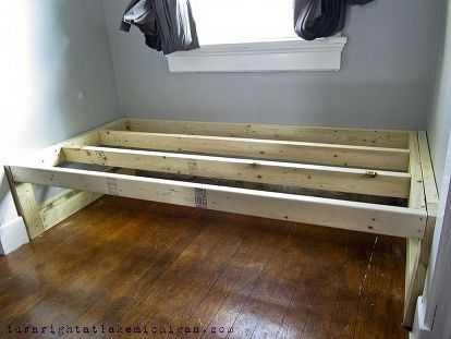 a wooden bed frame sitting on top of a hard wood floor next to a window