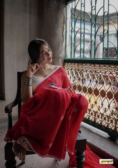 a woman sitting in a chair talking on a cell phone while wearing a red dress