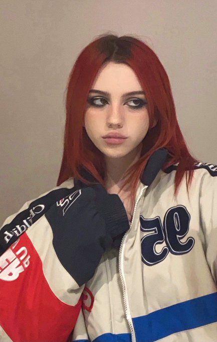 a woman with red hair and black eyeliners is wearing a jacket that has the number 95 on it