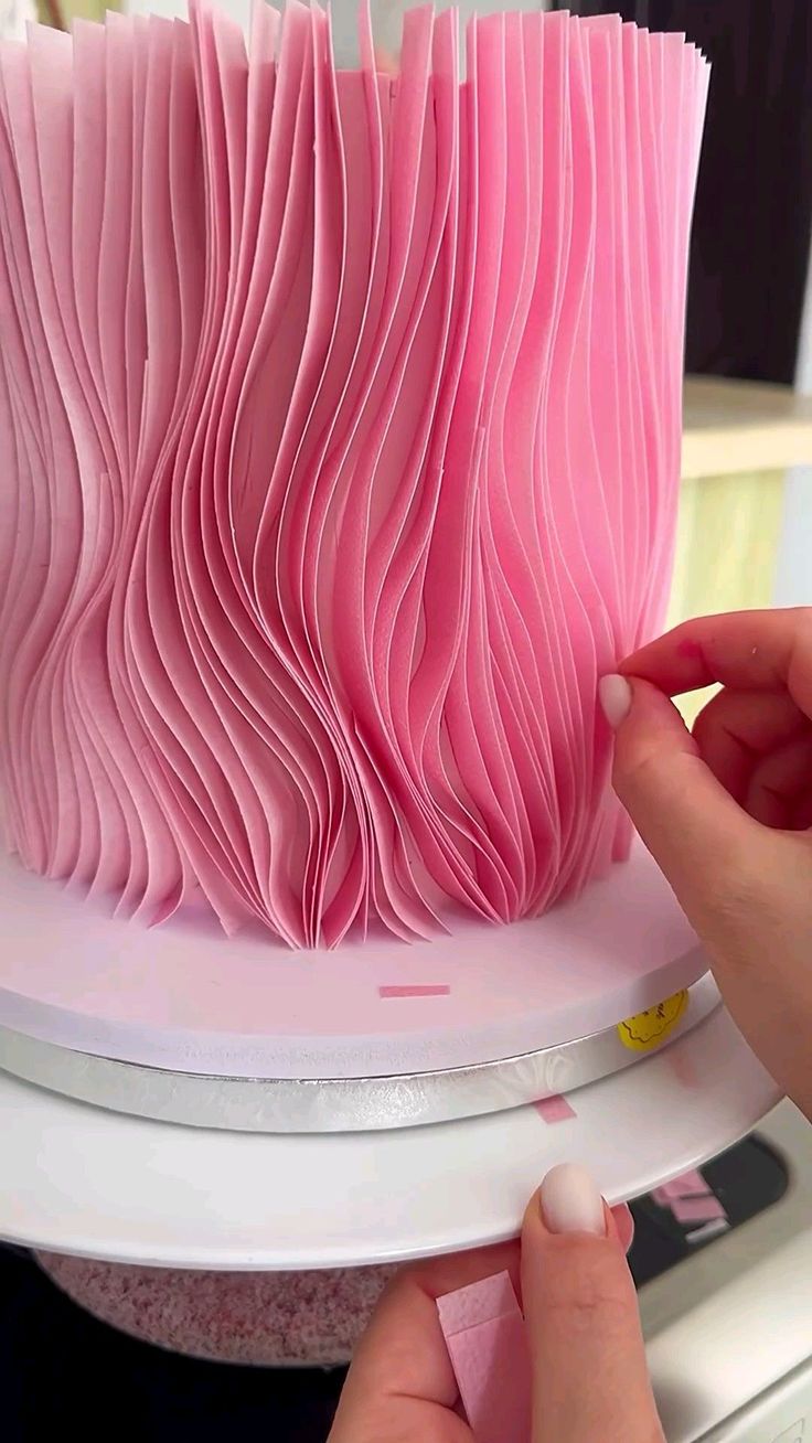 a woman is decorating a pink cake with icing