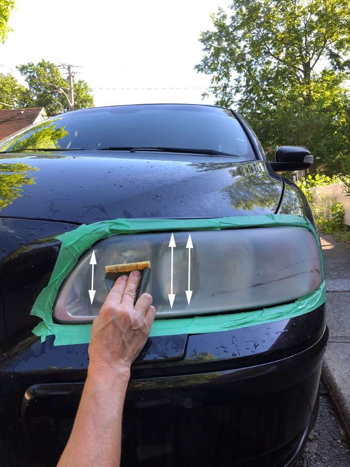 someone is cleaning the hood of a black car with green tape and an adhesive sticker