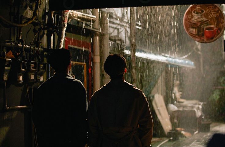 two men standing in the rain under an umbrella