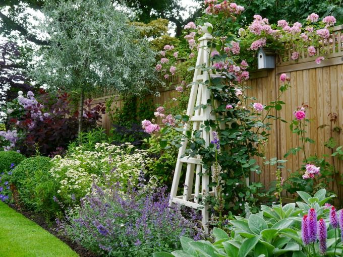 a garden with lots of flowers next to a wooden fence and some plants growing on it