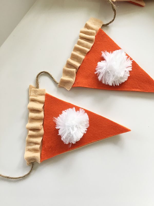 two pieces of felt with white pom poms on top of each other, hanging from twine strings