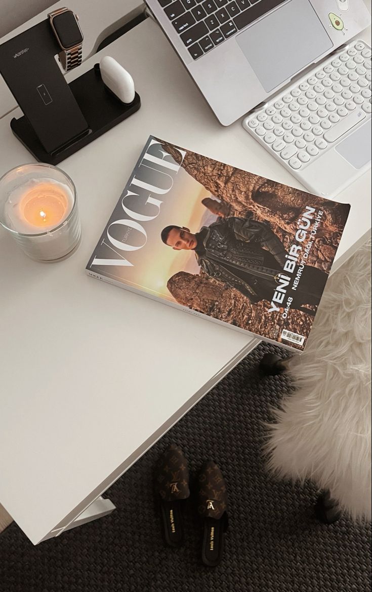 a magazine sitting on top of a white table next to a laptop computer and candle