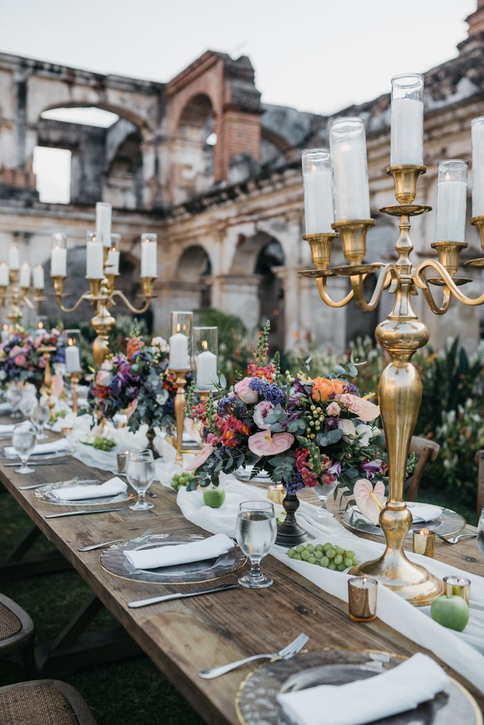 a long table with candles and flowers on it is set for an outdoor dinner party