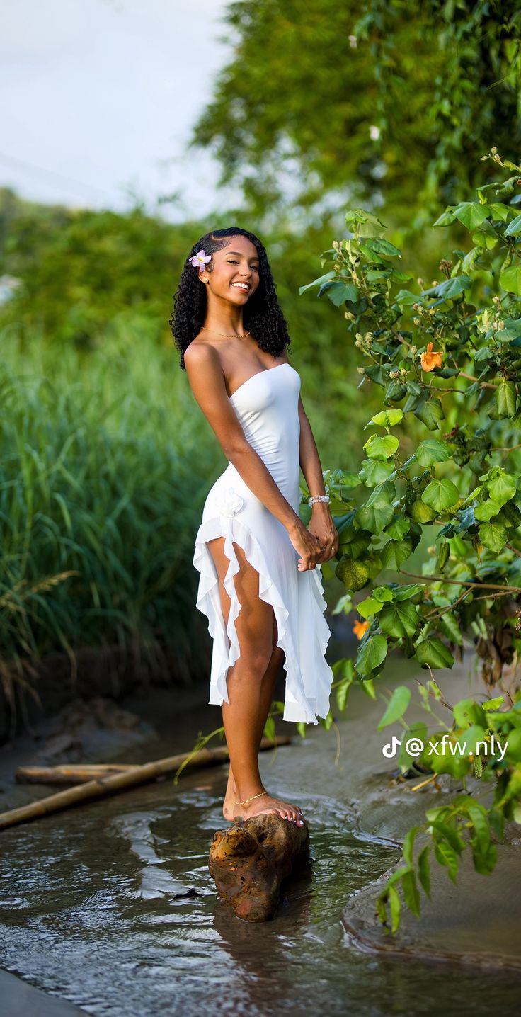 a woman in a white dress standing on top of a tree stump by the water