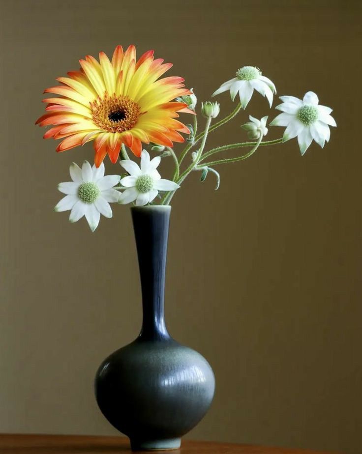 a black vase filled with white and orange flowers