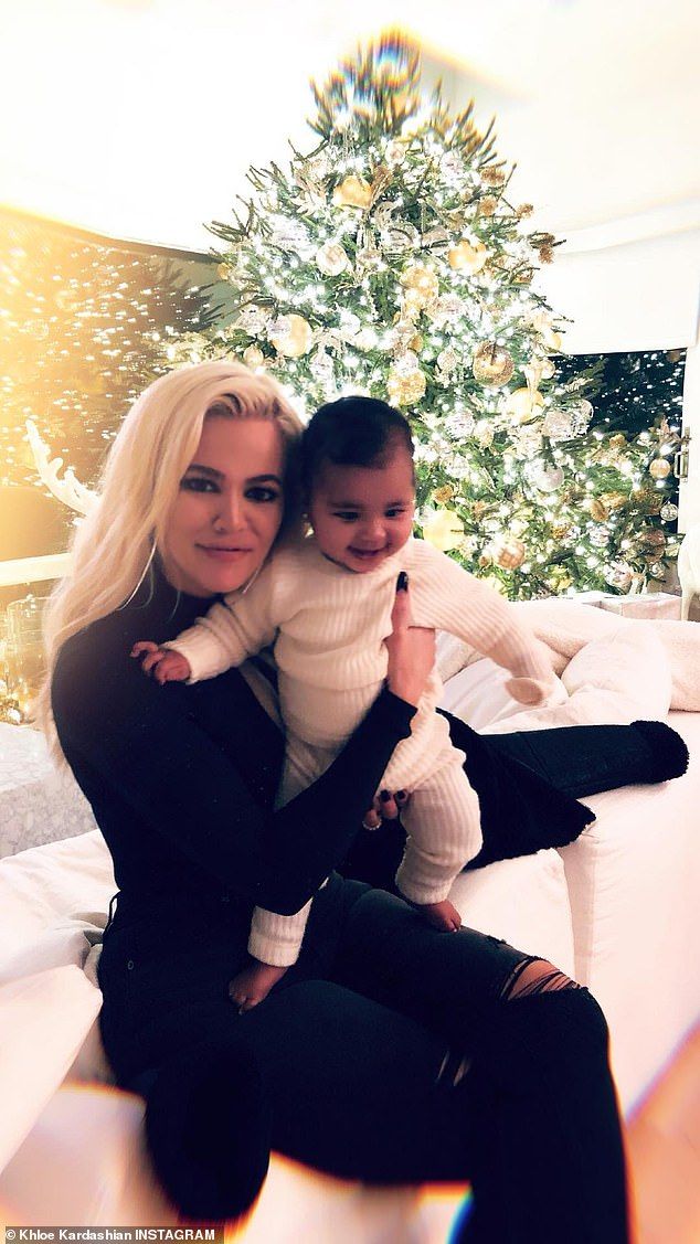 a woman holding a baby in her arms on top of a bed next to a christmas tree