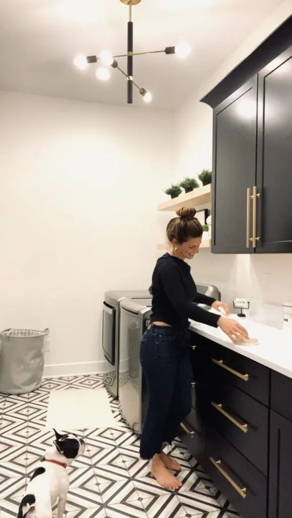 a woman standing in a kitchen next to a sink and two cats on the floor