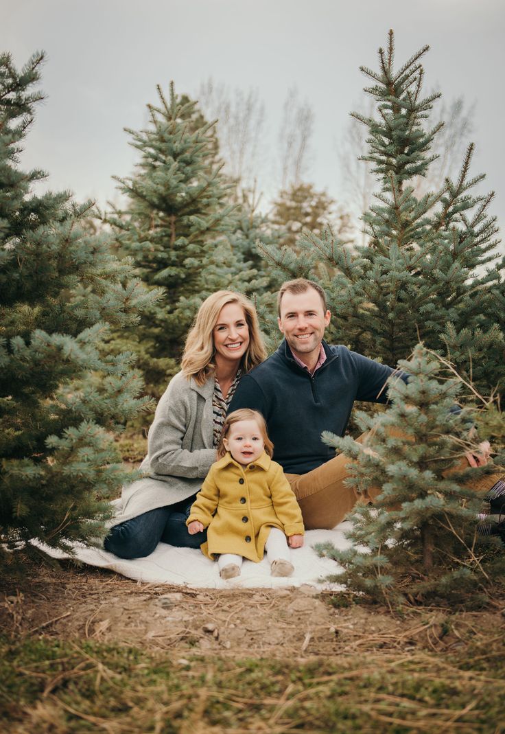 a man, woman and child are sitting in the middle of a christmas tree farm