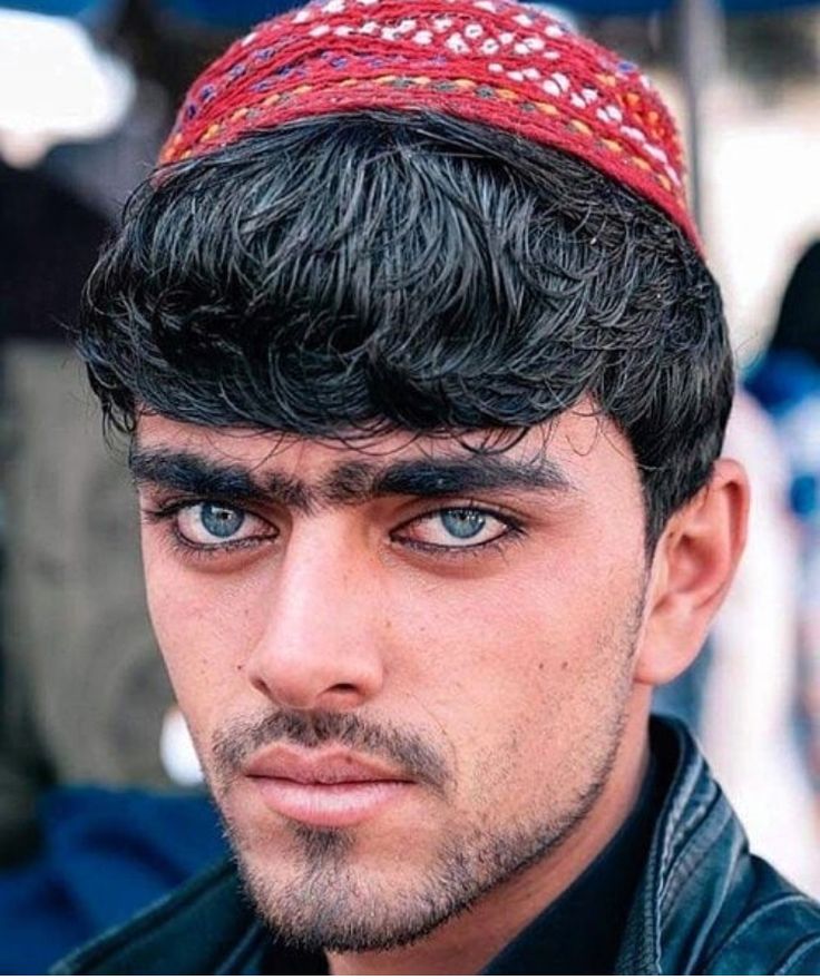 a close up of a person wearing a black jacket and a red headband with blue eyes