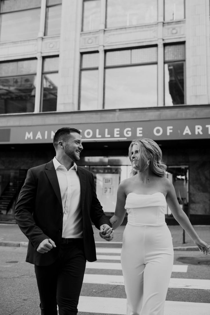 a man and woman walking across a street holding hands