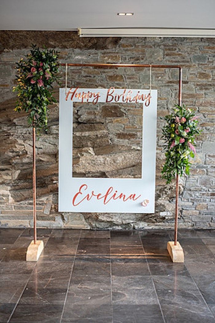 a photo frame decorated with flowers and greenery on the floor in front of a stone wall