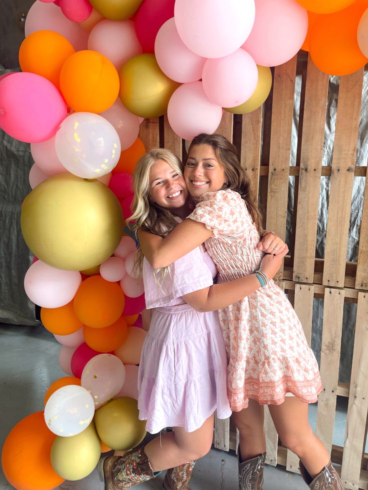 two girls hugging each other in front of balloons