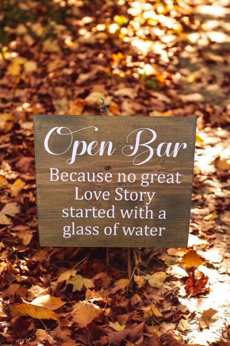 an open bar sign sitting on top of leaves in the woods with words written below it