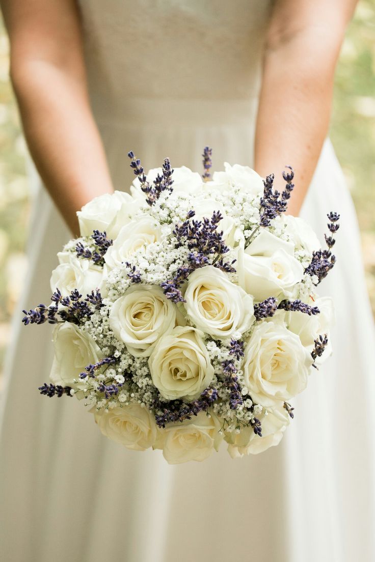 a bride holding a bouquet of white roses and lavenders