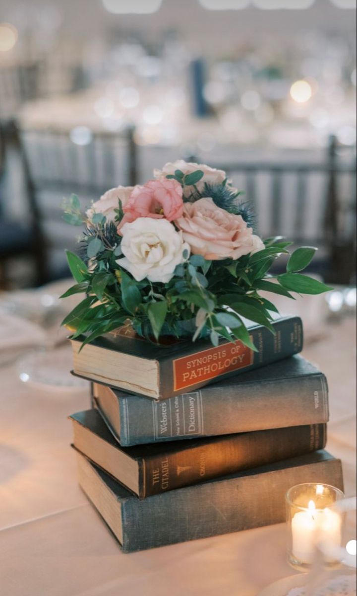 three books stacked on top of each other with flowers in the middle and candles lit behind them