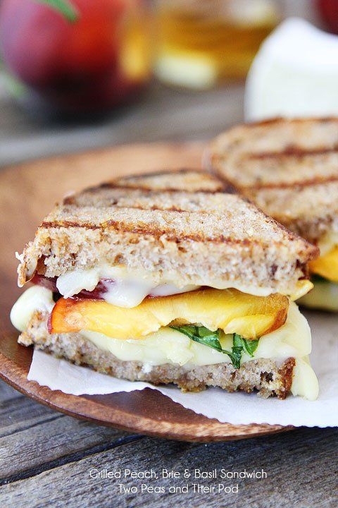 a grilled cheese and tomato sandwich on a wooden plate next to some fruit, with a glass of apple cider in the background