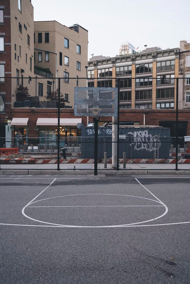 an empty basketball court in the middle of a city with lots of buildings behind it