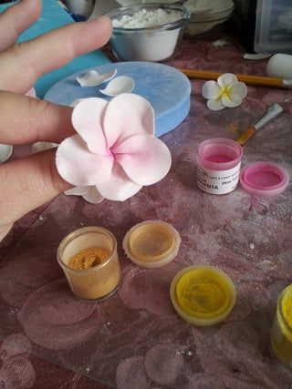 a person holding a flower in their hand next to some paint and other things on the table