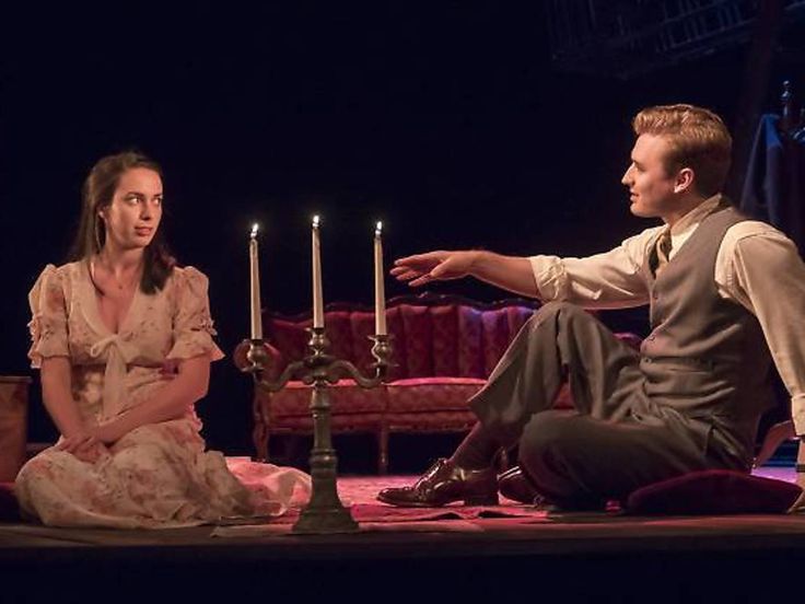 a man and woman sit on the floor in front of candles with one hand out