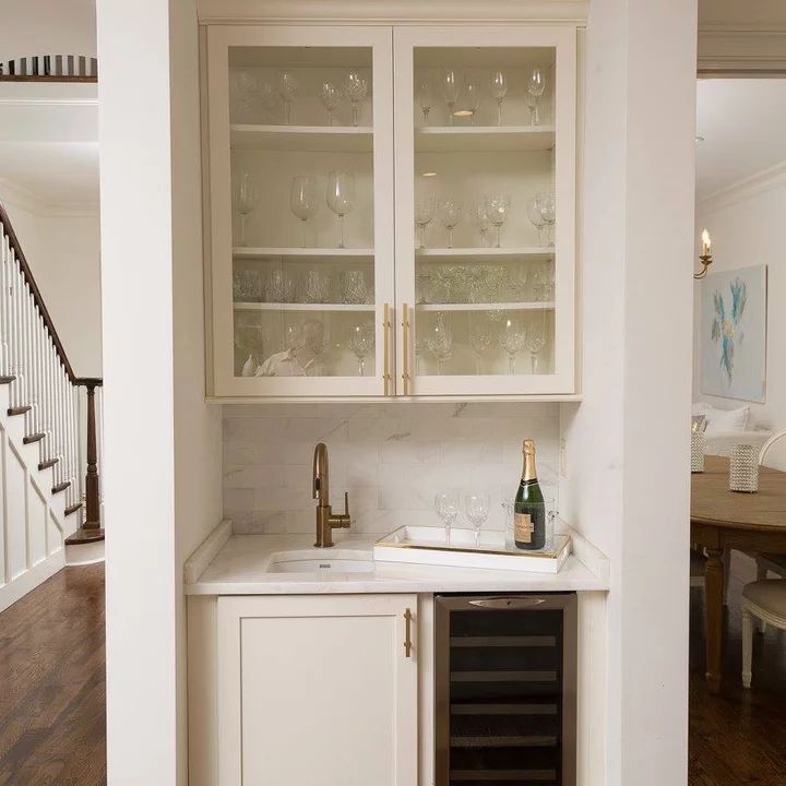 a kitchen with white cabinets and wine glasses on the top shelf in front of it