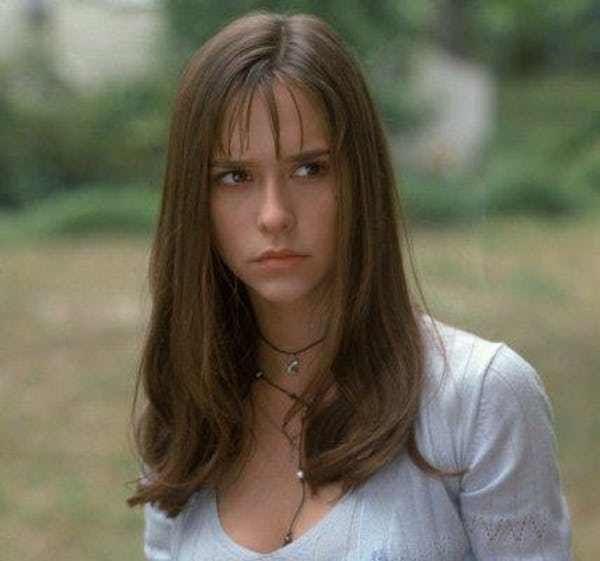 a young woman with long hair wearing a necklace and looking at the camera while standing in a field