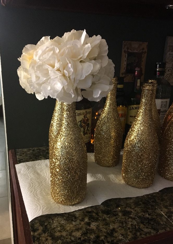 three gold vases with white flowers in them on a counter top next to bottles