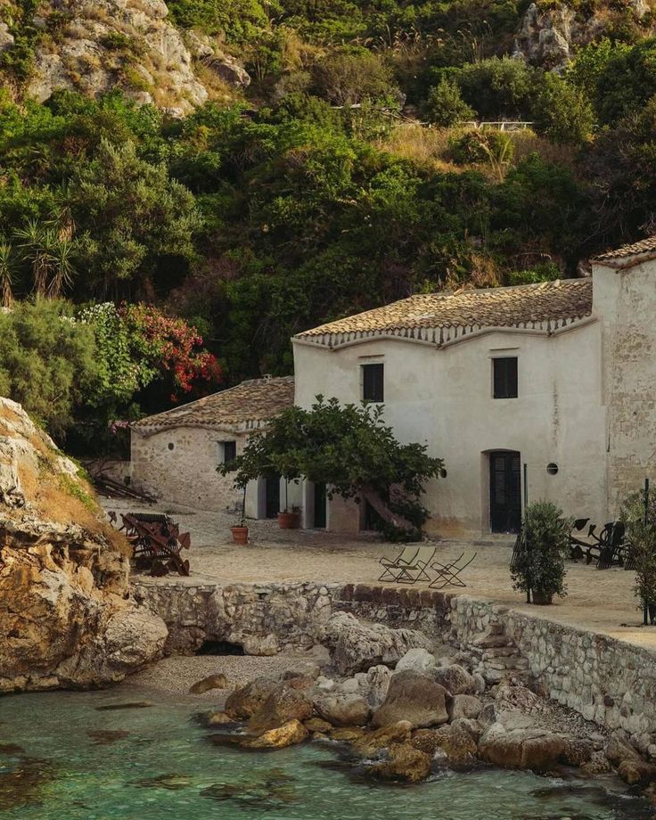 an old house sitting on the side of a cliff next to a body of water