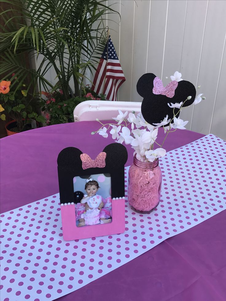 a minnie mouse photo frame sitting on top of a table next to a vase filled with flowers