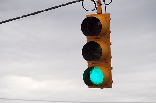 a green traffic light hanging from a wire on a cloudy gray day with power lines in the background