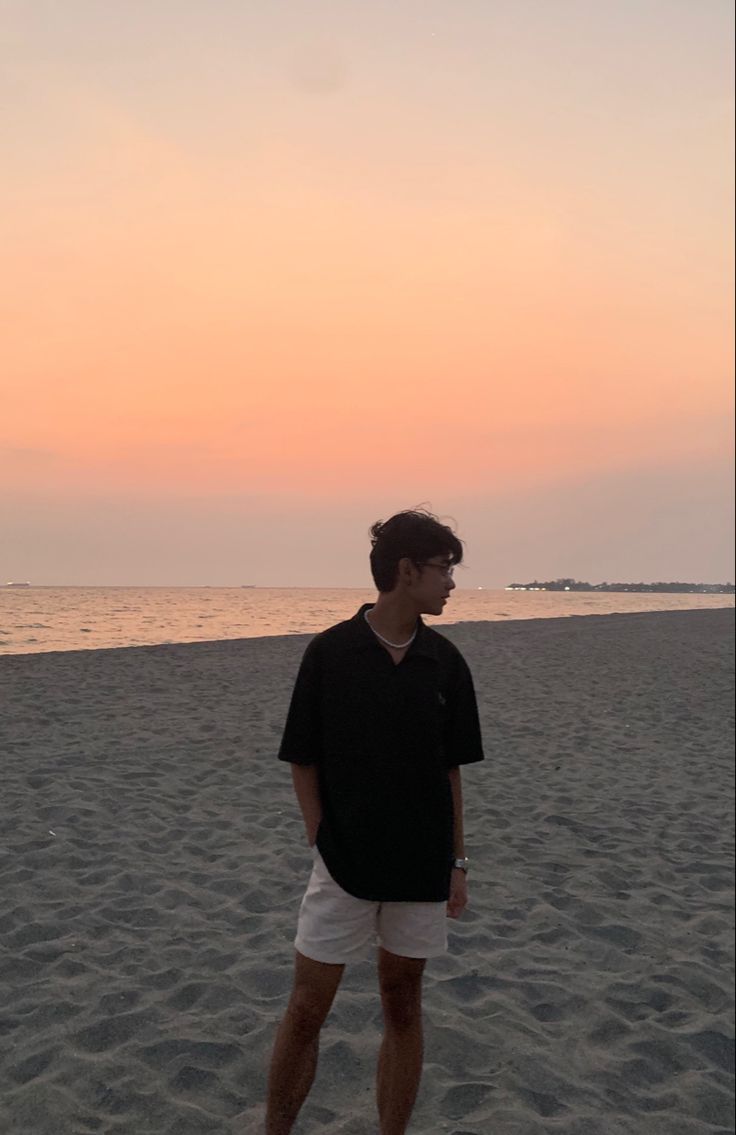 a man standing on top of a sandy beach next to the ocean under a pink sky