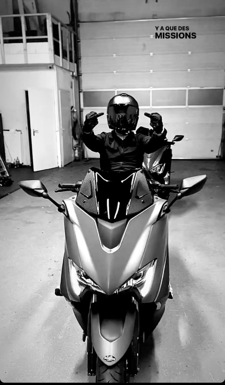 a man riding on the back of a silver motorcycle in a garage with his hands up