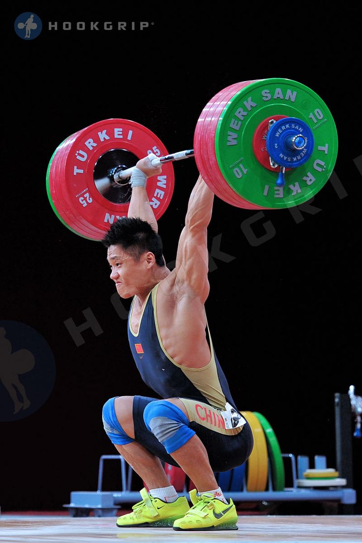 a man squats with a barbell in front of his head while holding a weight plate