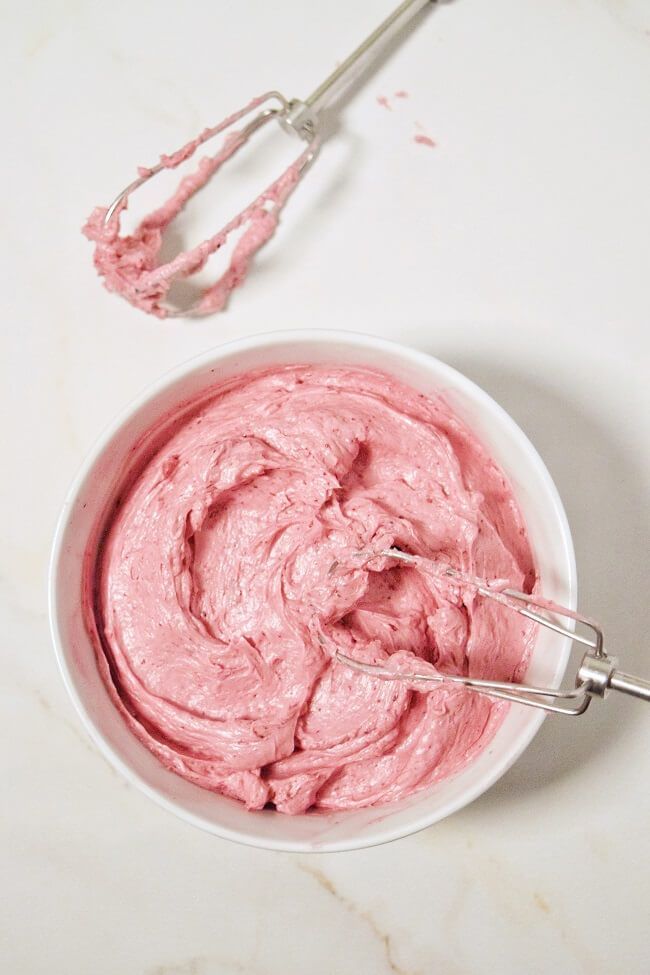 a bowl filled with pink whipped cream next to a whisk on a counter