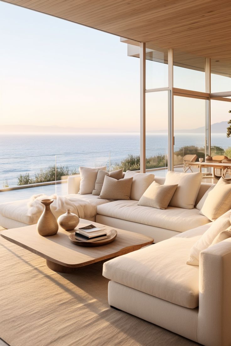 a living room filled with furniture next to a large window overlooking the ocean on a sunny day