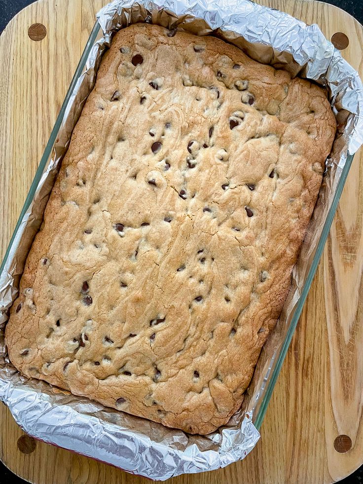 a cookie cake sitting on top of a wooden cutting board next to a glass container