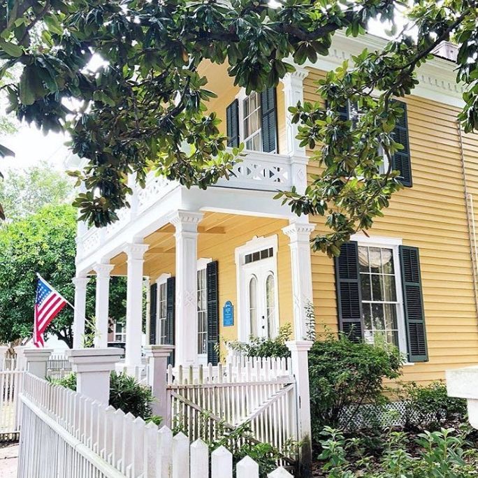 a yellow house with black shutters and an american flag on the porch