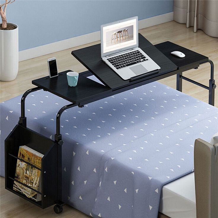 a laptop computer sitting on top of a table next to a bed with a blue sheet