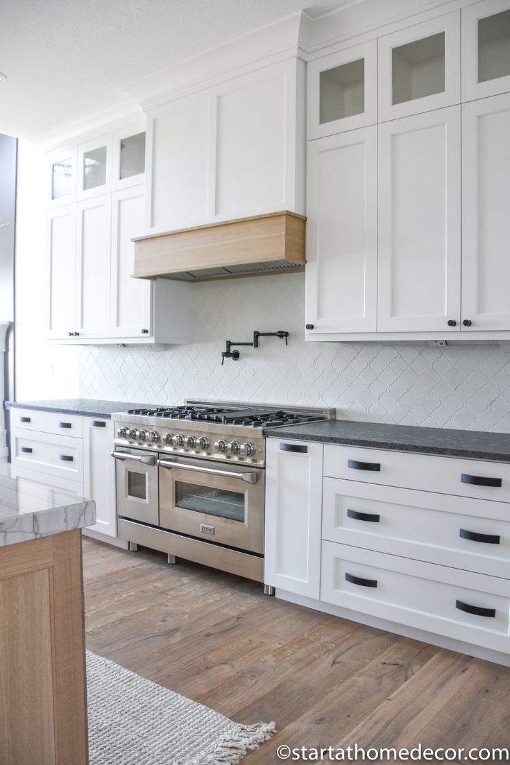 a kitchen with white cabinets and stainless steel stove top oven in the middle of it