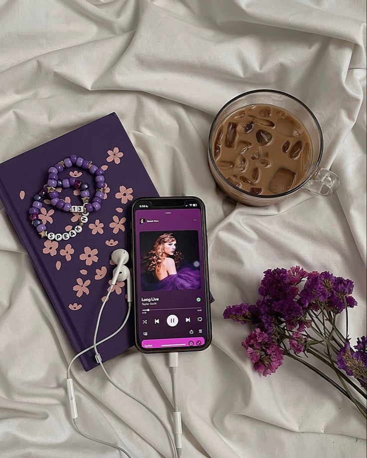 an mp3 player and book on a bed next to some purple flowers with headphones