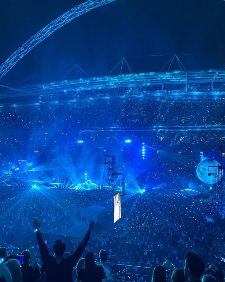 a large crowd at a concert with their hands up in the air and lights on